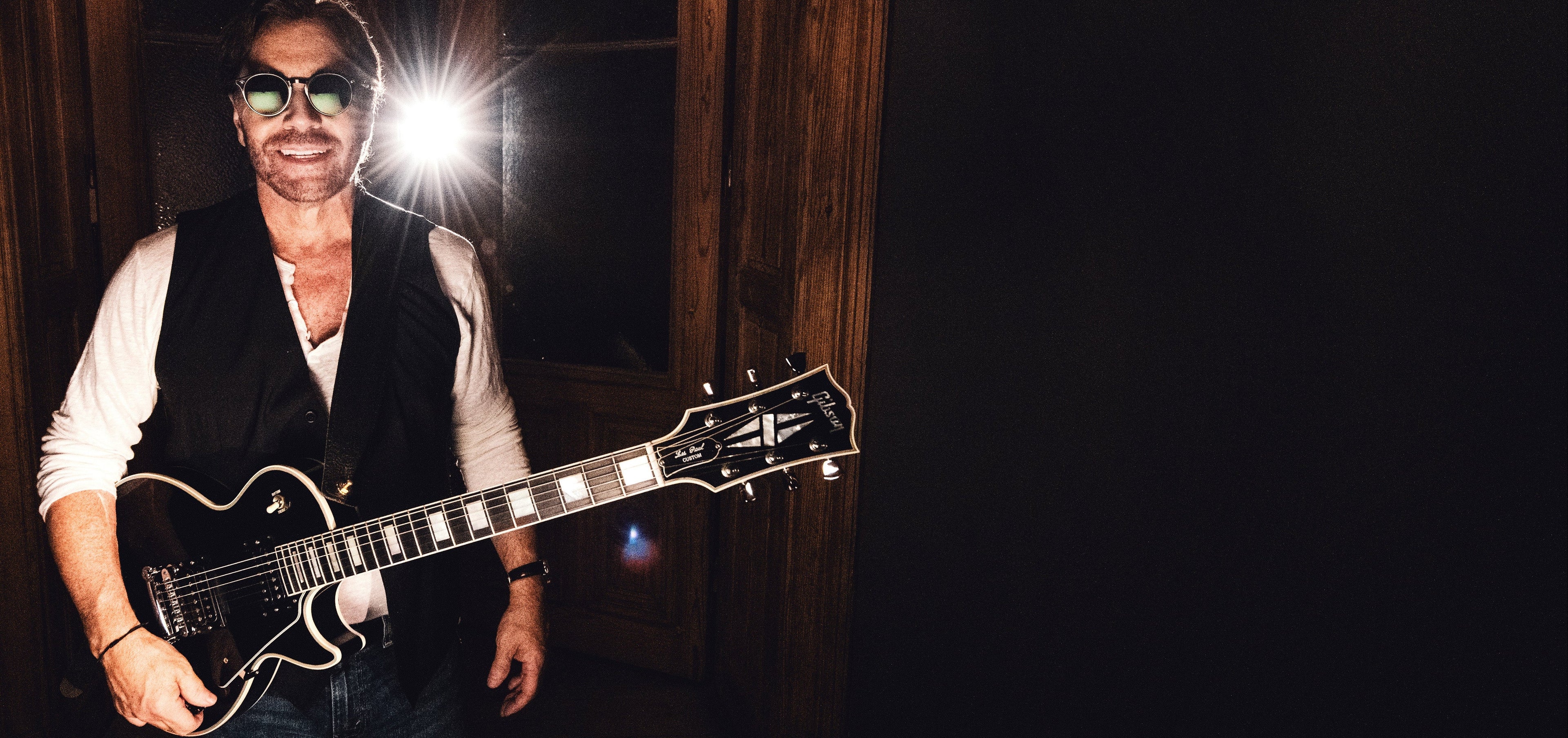 Al Di Meola holding a guitar in a dimly lit back-stage area